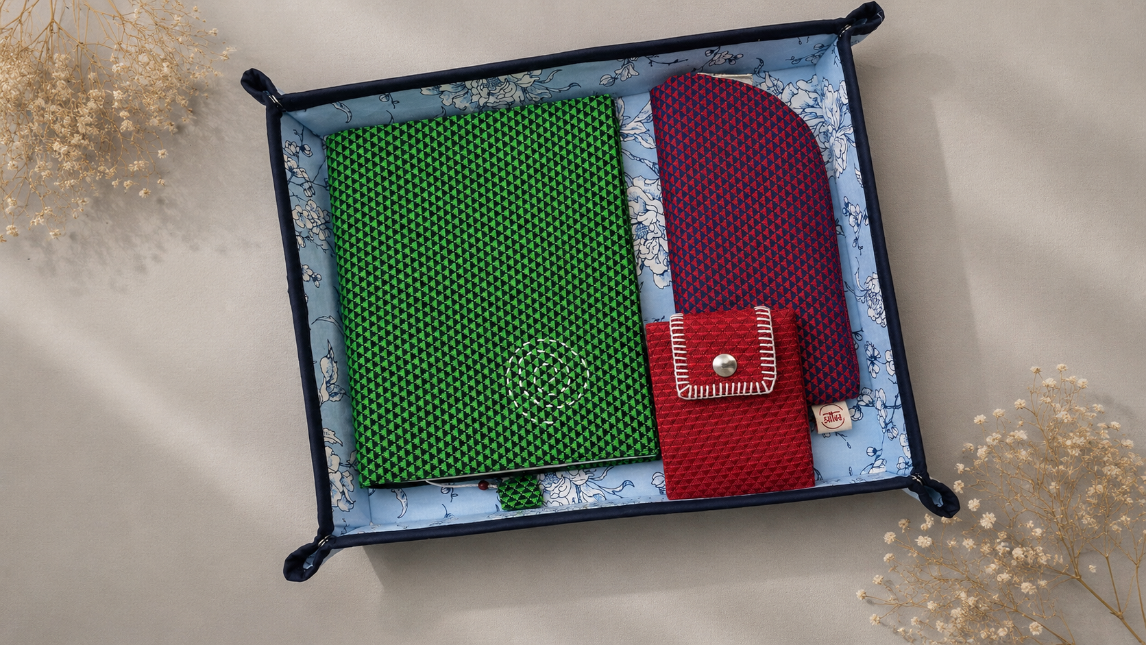 A gift set of three textured fabric accessories , Daily Journal in Khun fabric in green,Card wallet in red Khun Fabric, and eyewear pouch in Khun fabric in magenta, presented in an upcycled fabric tray that is foldable 